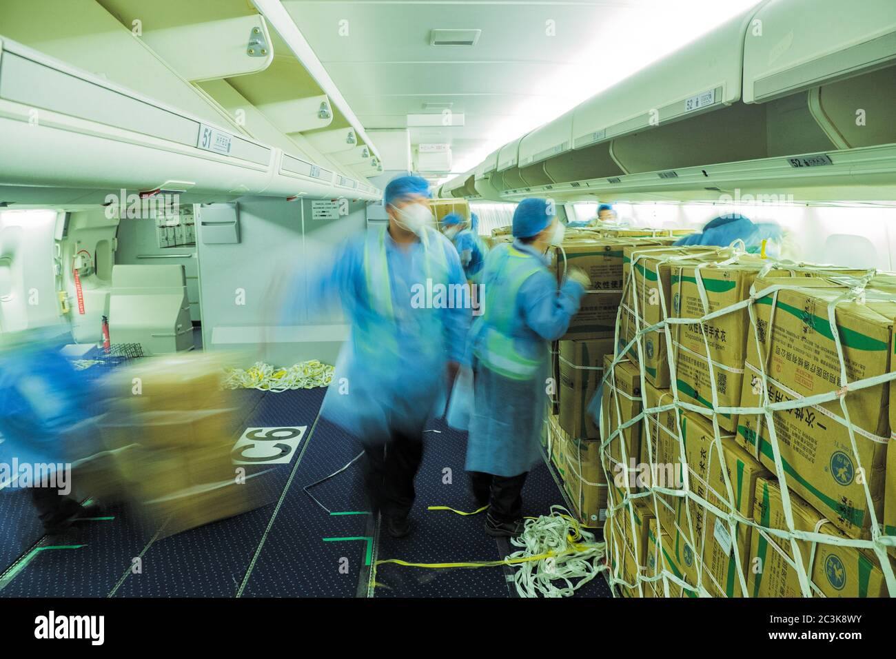 Caricatori cinesi che indossano abiti da muta caricando un passeggero convertito in aereo da freighter con maschere chirurgiche e camici per combattere il Pandemia COVID Foto Stock