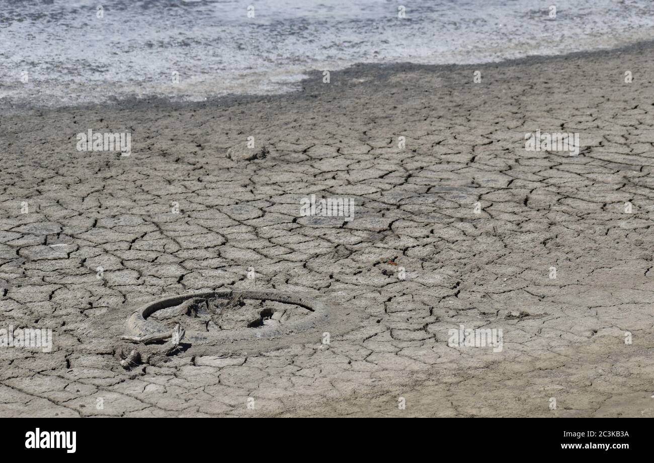 Un vecchio pneumatico, incastonato nel fango incrinato del lago morente, con una crosta di sale al bordo dell'acqua Foto Stock