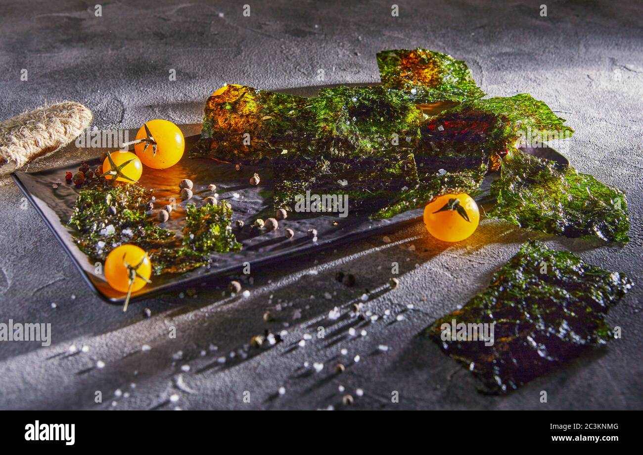 Alghe nori croccanti con pomodori ciliegini e spezie scure su cemento grigio. Cibo giapponese nori. Fogli secchi di alghe. Spazio di copia. Foto Stock