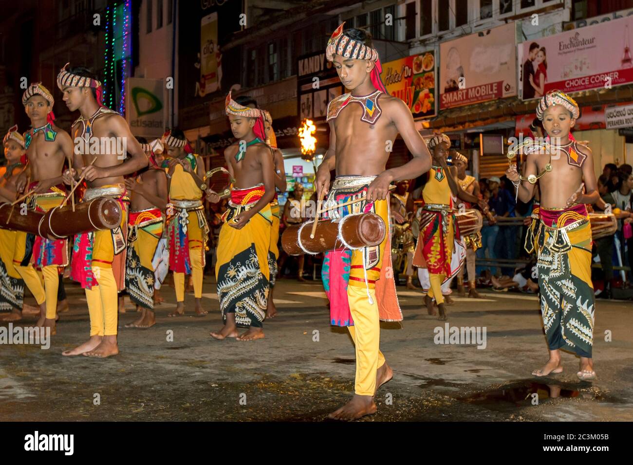 Giovani musicisti, tra cui batteristi e suonatori di tamburelli, si esibiscono lungo una strada a Kandy in Sri Lanka durante l'Esala Perahera. Foto Stock