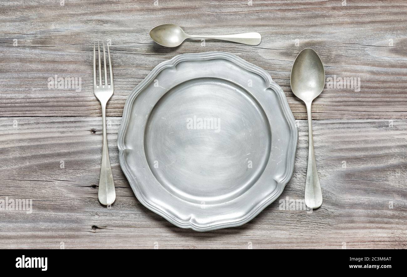 Forchetta, cucchiai e piatto di peltro vintage su vecchie tavole di legno Foto Stock