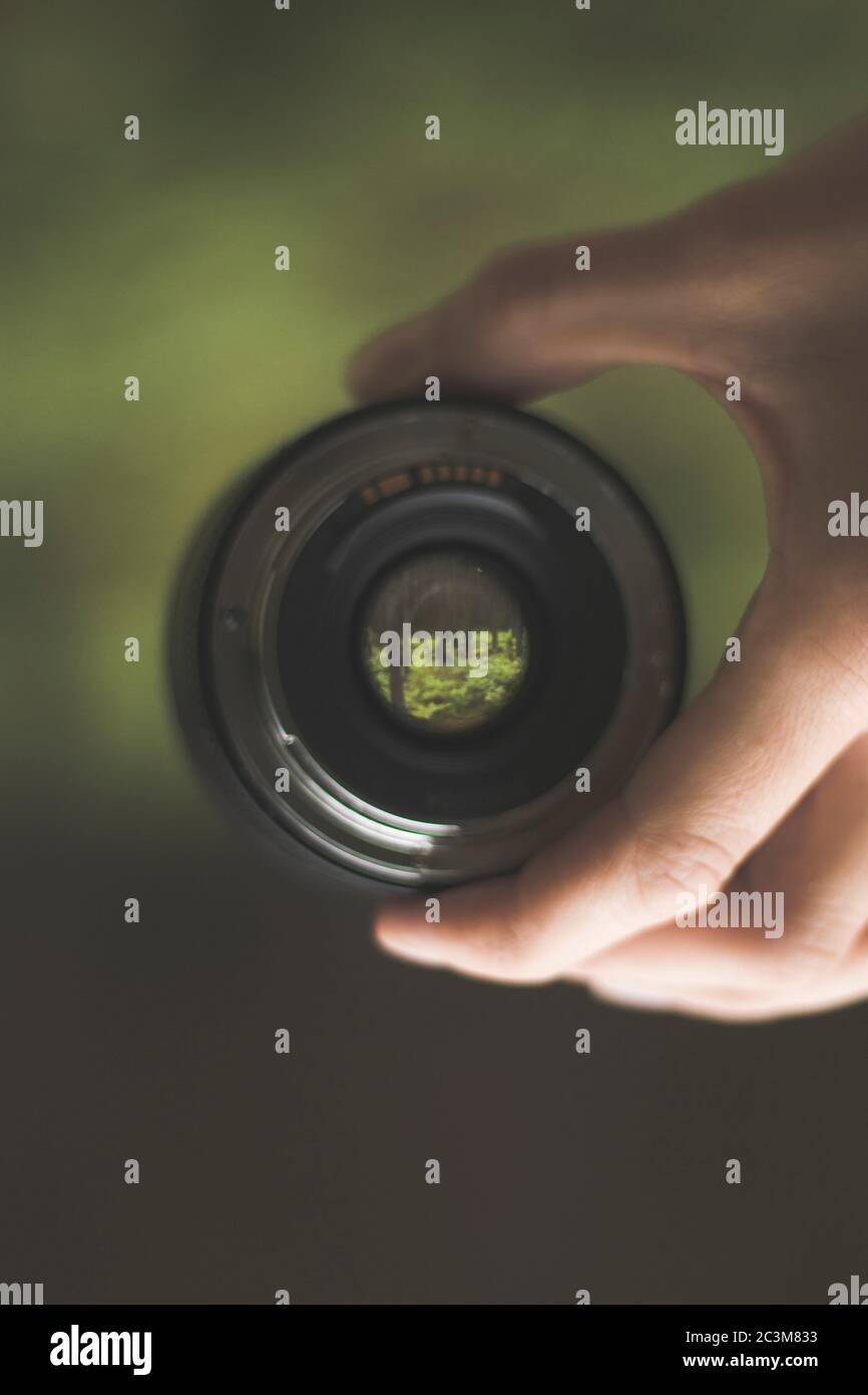 Primo piano della mano di una persona che tiene un obiettivo della fotocamera su uno sfondo sfocato Foto Stock