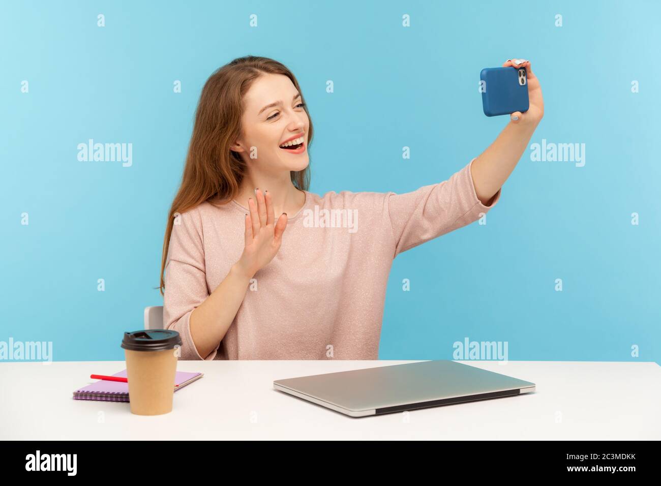 Donna, dipendente o blogger ottimista e amichevole, seduto sul posto di lavoro e prendendo selfie dal telefono cellulare, parlando in videochiamata e salutando Foto Stock