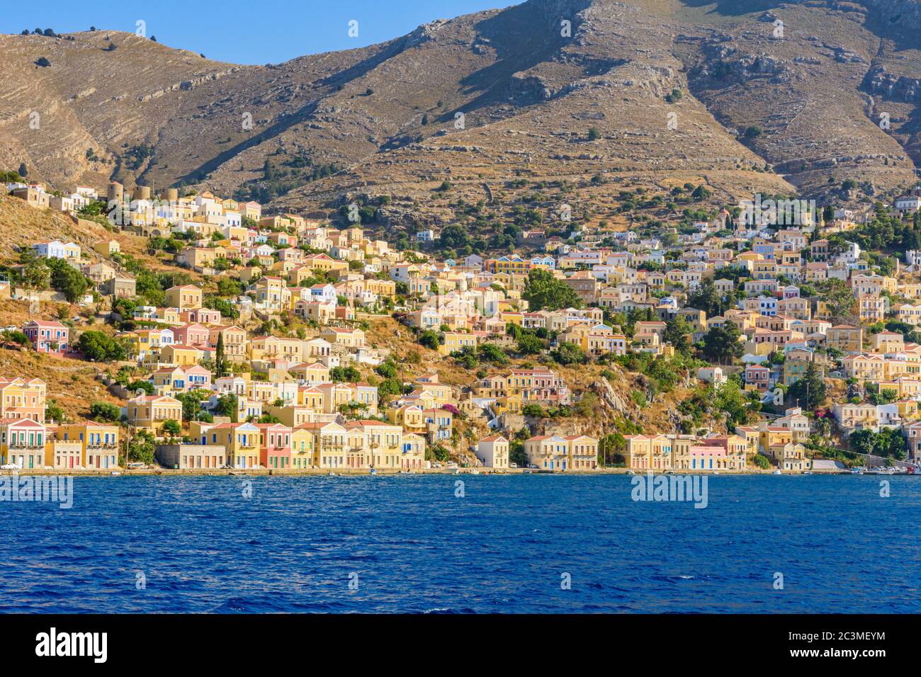 Sole nel tardo pomeriggio sulle ville neo-classiche del porto di Gialos e la vecchia collina Horio, isola di Symi, Dodecanese, Grecia Foto Stock