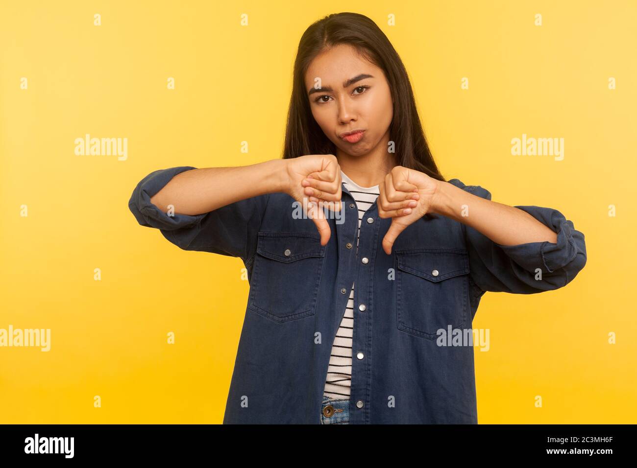 Risultato terribile! Ritratto di ragazza insoddisfatta in camicia denim mostrando pollici giù, segno di disapprovazione, gesturing non piace a cattivo servizio, in disaccordo con sugg Foto Stock