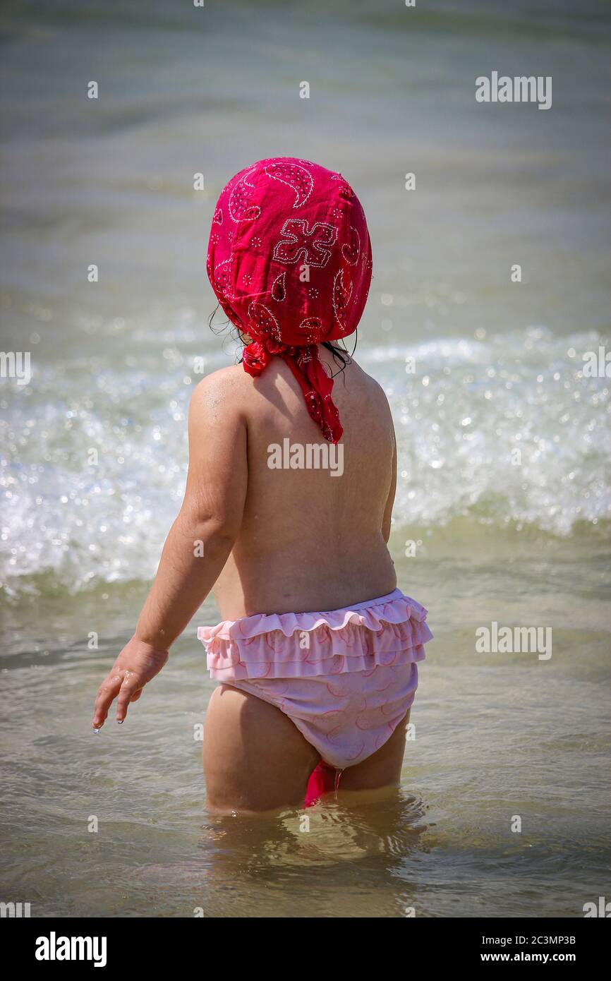 Una bambina carina e dolce gioca con acqua e sabbia sulla riva. Bambino con  costume da
