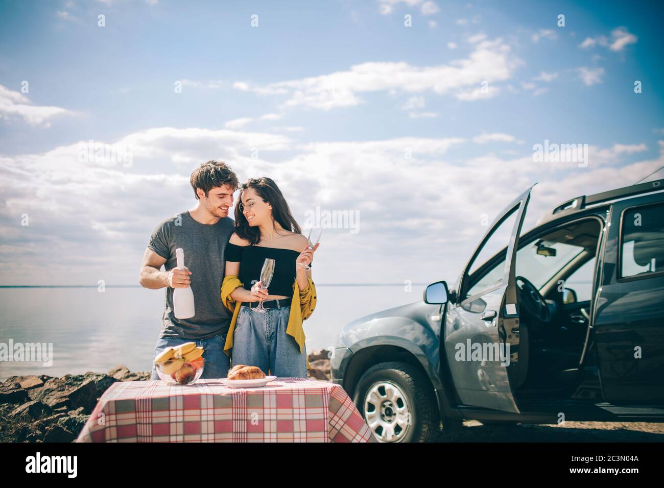 Picnic vicino all'acqua. Buona famiglia in viaggio in auto. L'uomo e la donna viaggiano in riva al mare, all'oceano o al fiume. Giro estivo in auto Foto Stock