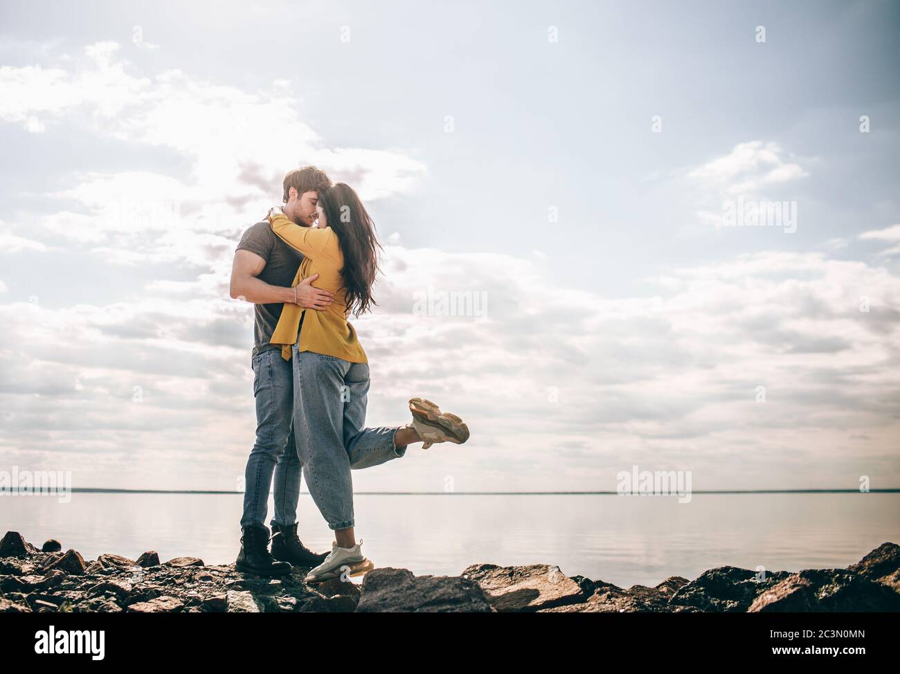 Amore e viaggio. Una coppia si trova sullo sfondo della baia. Un uomo e una donna stanno in piedi vicino a un fiume o mare su pietre e abbracciando Foto Stock