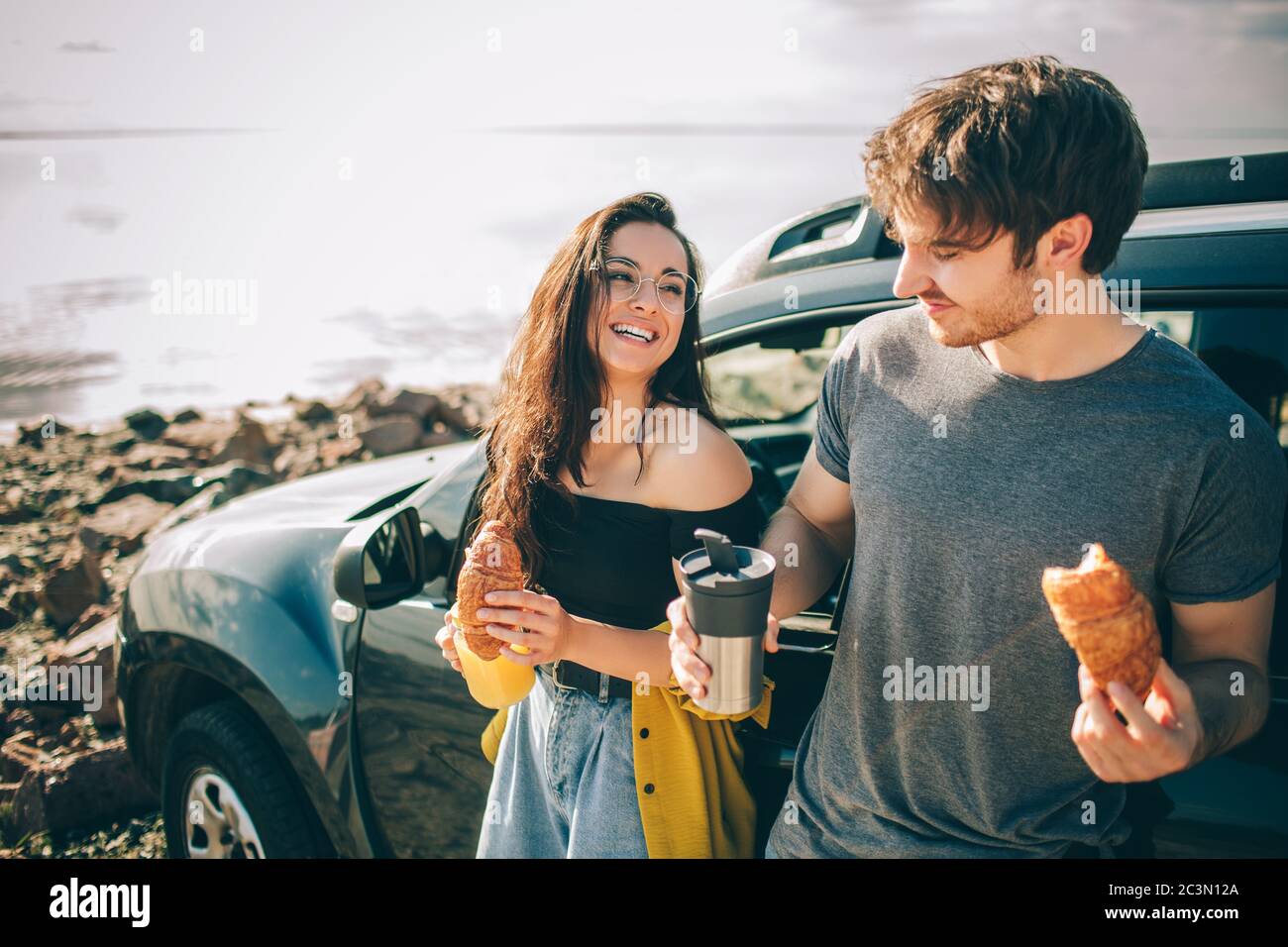 Picnic vicino all'acqua. Buona famiglia in viaggio in auto. L'uomo e la donna viaggiano in riva al mare, all'oceano o al fiume. Giro estivo in auto Foto Stock