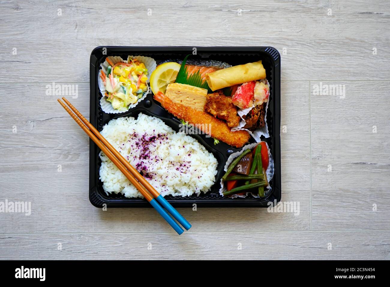 Scatola giapponese bento colorata con riso, gamberi fritti, salmone, involtino primaverile, verdure, tofu e pollo. Tavolo di legno sfondo. Foto Stock