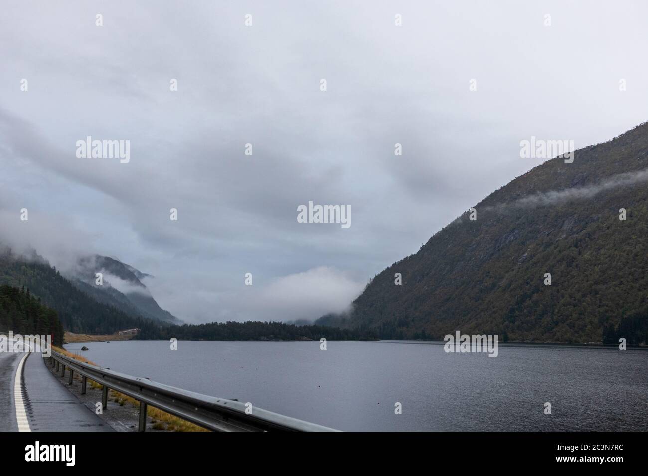 Strada statale in un lago di montagna nebby in Norvegia. Autunno pittoresca nebbia basse nuvole sulla strada per Oslo in una mattinata piovosa bagnato Foto Stock