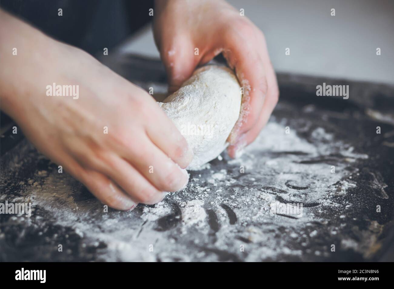 Su una teglia scura, cosparsa di farina, un uomo impastò con le mani per preparare la pizza fatta in casa. Il processo di cottura a casa. Foto Stock