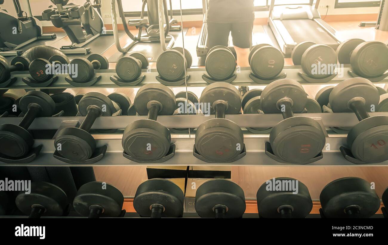 Set di manubri neri. Primo piano molti manubri in metallo su rack nel centro fitness sportivo, concetto di attrezzature per l'allenamento dei pesi. Foto Stock