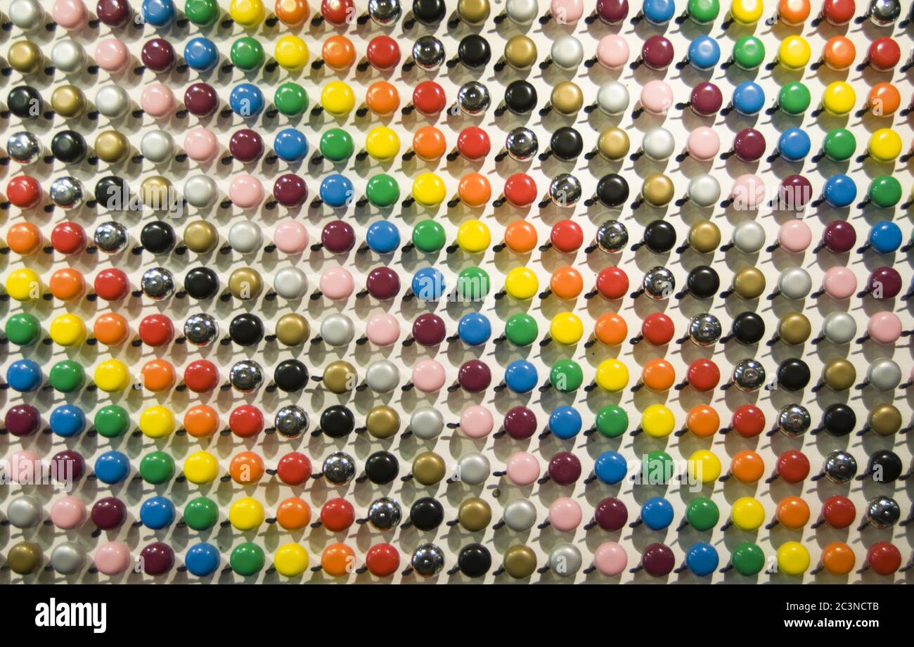 Collezione di campane di biciclette colorate in un modello su un parete bianca Foto Stock