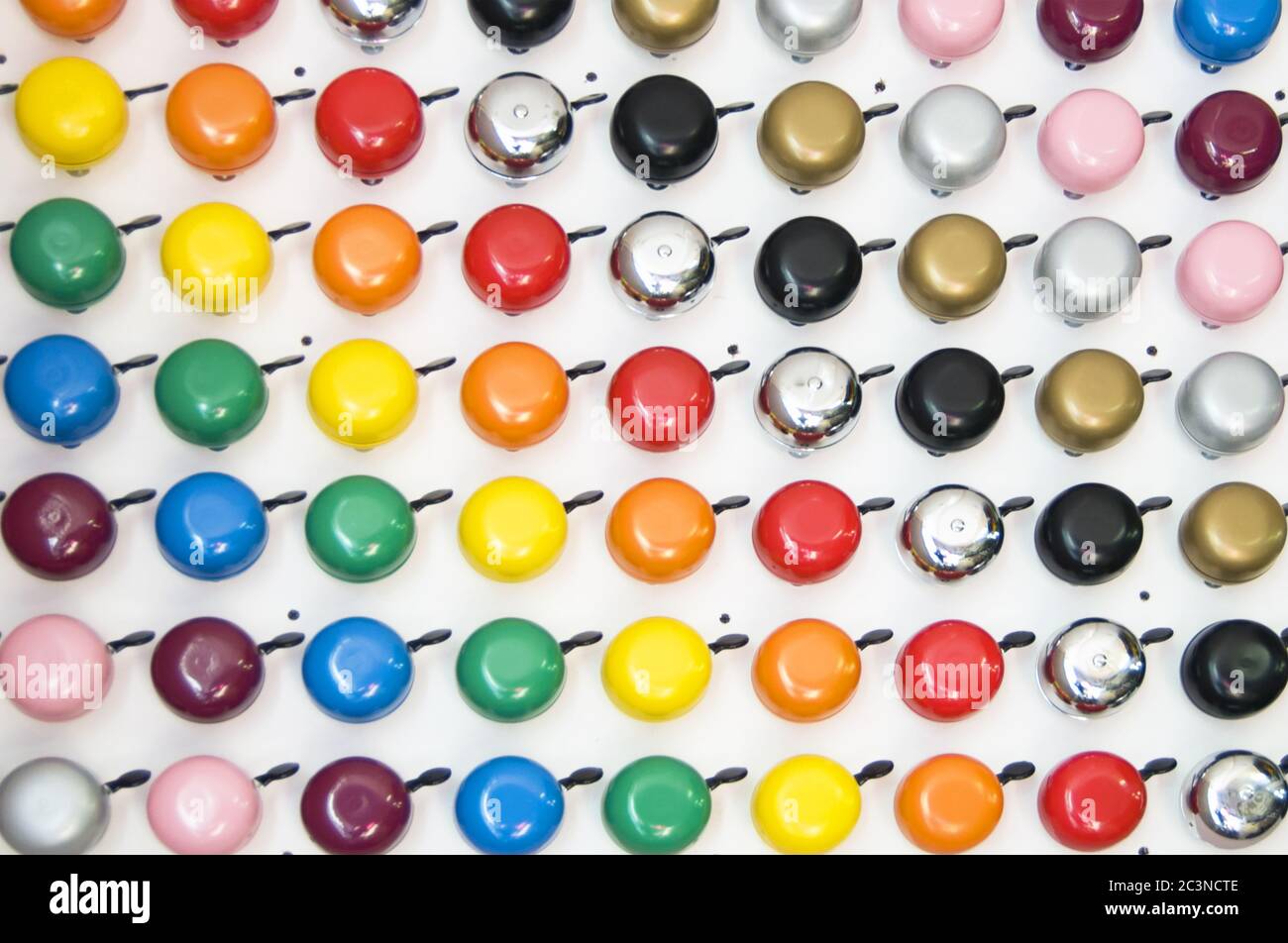 Collezione di campane di biciclette colorate in un modello su un parete bianca Foto Stock