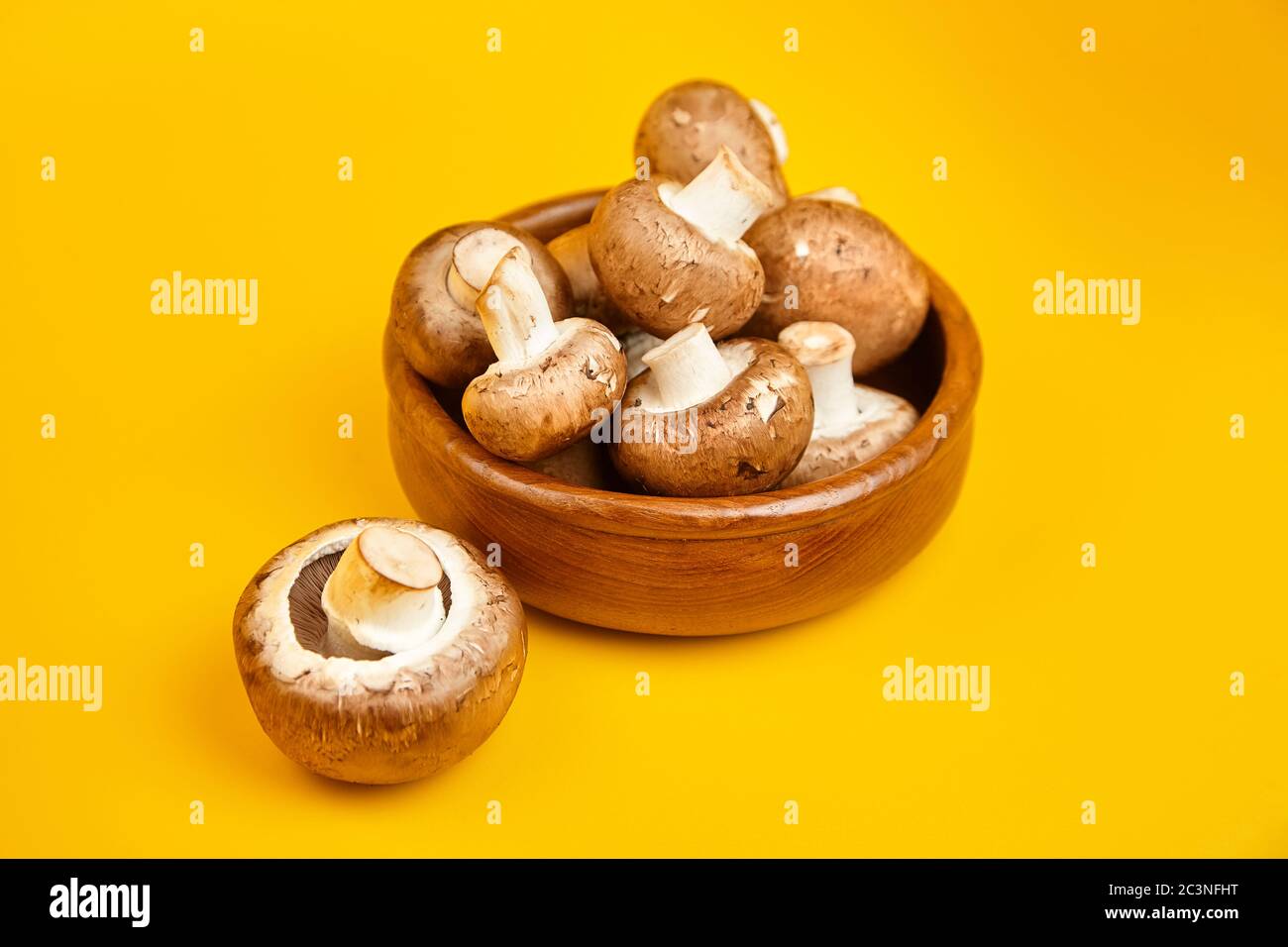 Funghi in ciotola di legno, champignons marroni freschi su fondo giallo. Ingrediente alimentare crudo Foto Stock