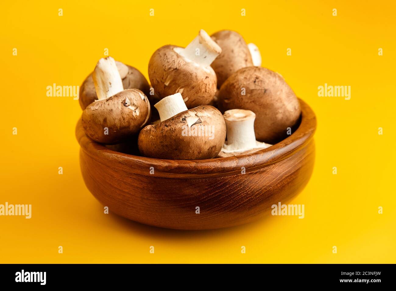 Funghi in ciotola di legno, champignons marroni freschi su sfondo giallo, fuoco selettivo. Ingrediente alimentare crudo Foto Stock