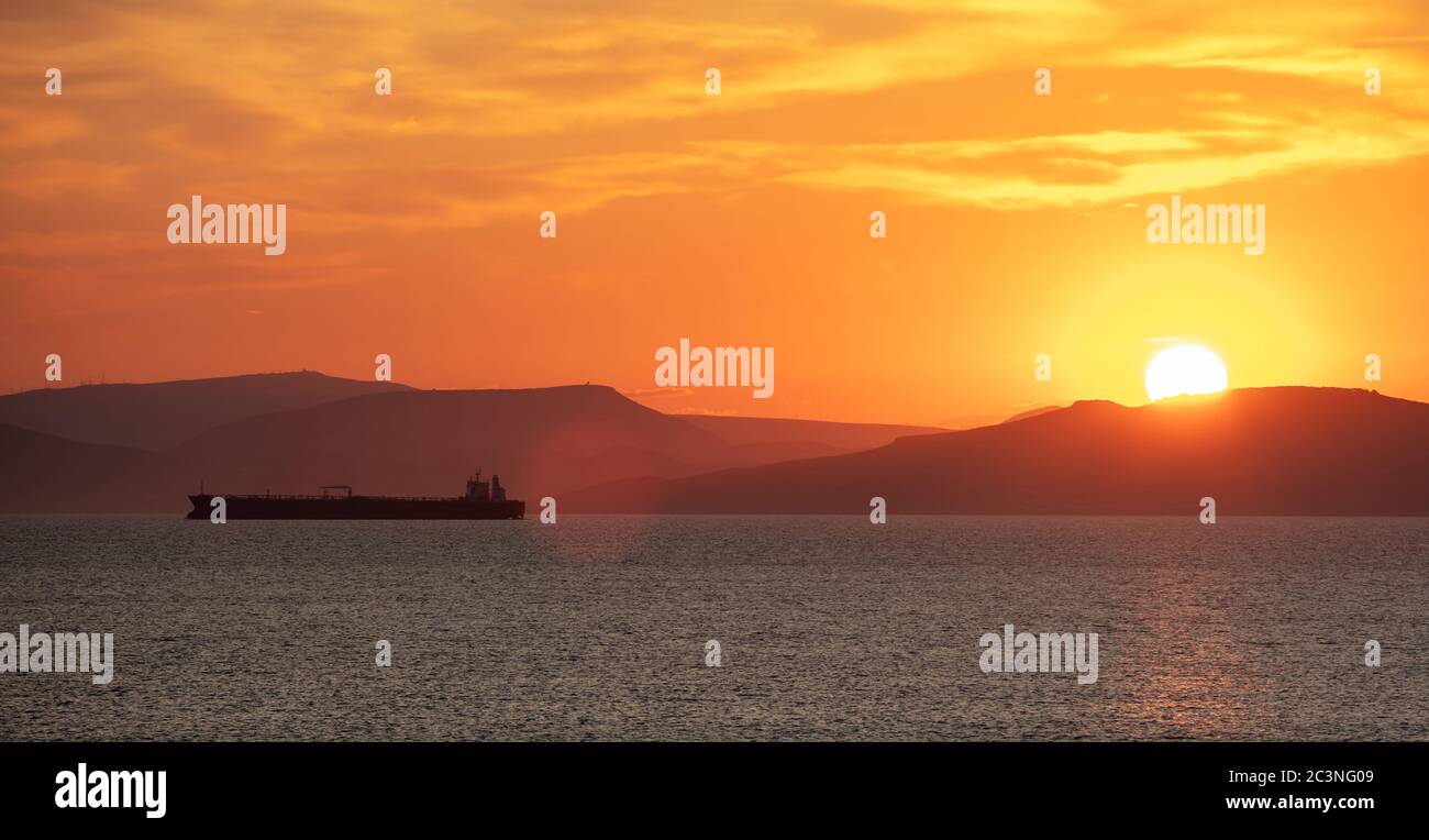 Tramonto arancione nuvoloso paesaggio sull'acqua di mare. Spettacolare e magico tramonto mare in Grecia mar Egeo. Crepuscolo, sfondo dell'alba. Terra e orang dell'isola oscura Foto Stock