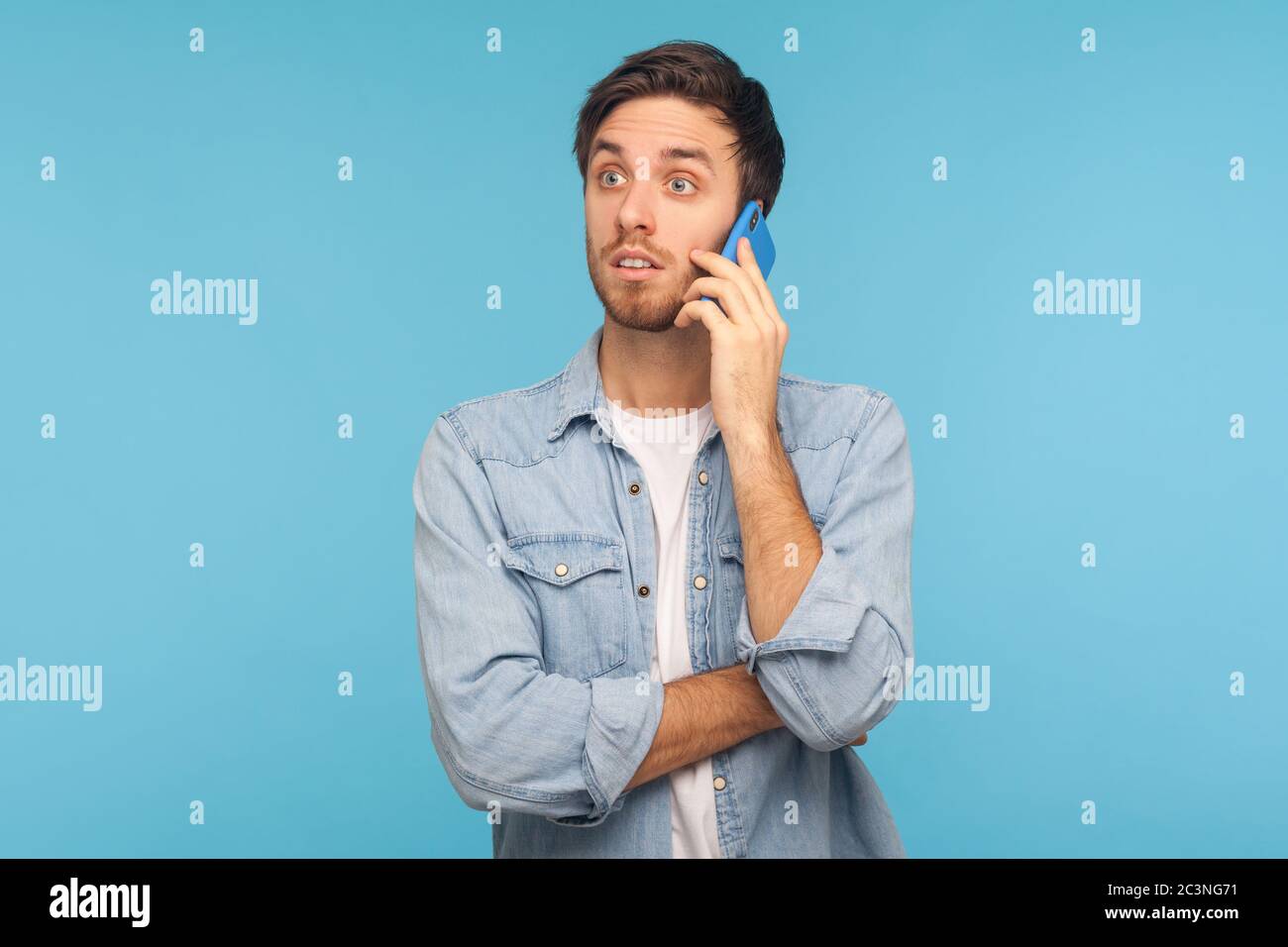 Ritratto di giovane uomo d'affari stupito in camicia casual denim che parla al telefono e l'aspetto scioccato, sorpreso da inaspettata conversazione mobile con parte Foto Stock