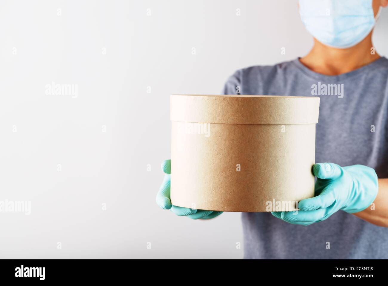 Un addetto al servizio di consegna può contenere una scatola con guanti e una maschera per proteggerla da virus e malattie su sfondo bianco. Foto Stock