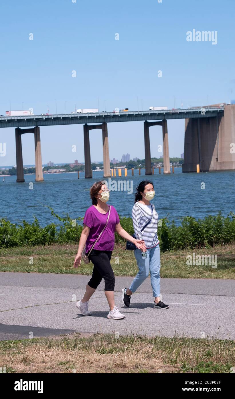 All'ombra del ponte sul collo di Throgs, 2 donne con una maschera chirurgica si esercitano a piedi su un sentiero nel Little Bay Park a Whitestone Queens, New York. Foto Stock