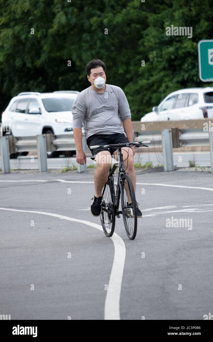 Un uomo asiatico americano, probabilmente coreano, biciclette su un percorso vicino alla Cross Island Parkway che indossa una maschera e casco. A Bayside, Queens, New York. Foto Stock