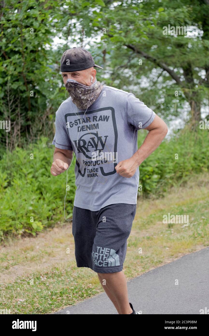 Un uomo che corre con una copertura di faccia bandana. Su un sentiero vicino alla Bayside Maina a Queens, New York City. Foto Stock