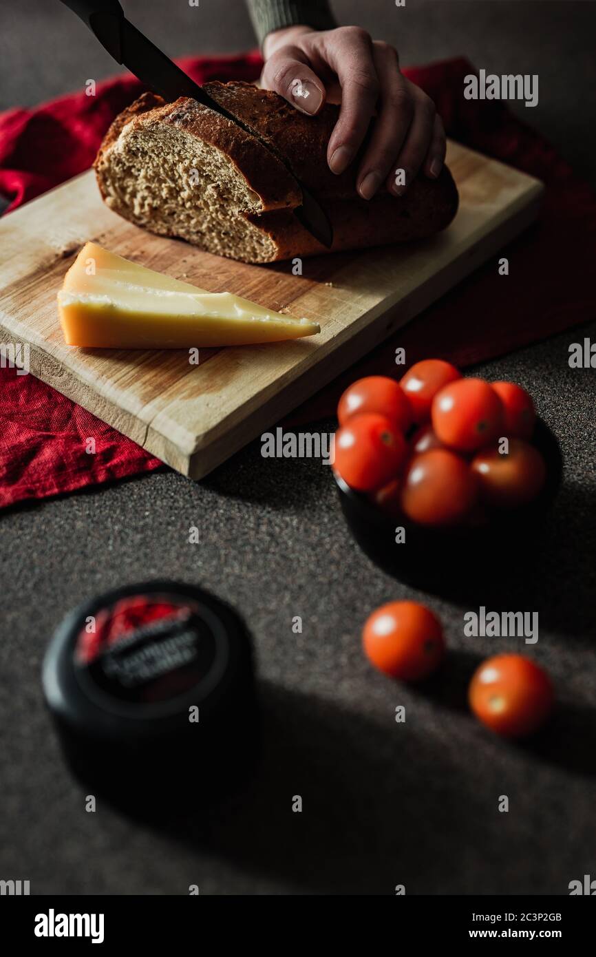 Donna che affetta pane di segale su un tagliere di legno. Un pezzo di  parmigiano, pomodori ciliegini, un piccolo camioncello di formaggio in  primo piano. Moody nat Foto stock - Alamy