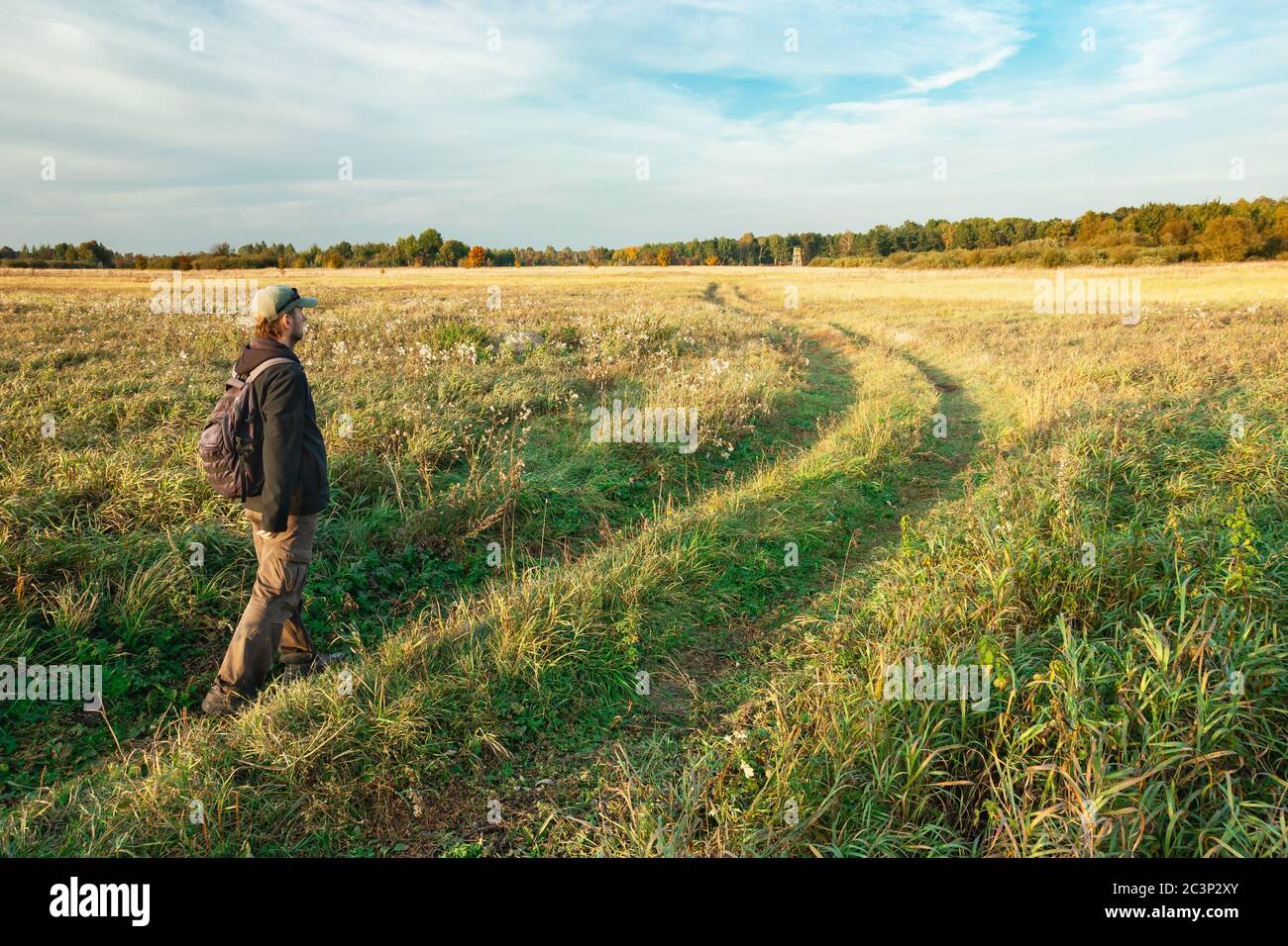 Un uomo con uno zaino che cammina lungo la strada erbosa attraverso i prati, vista della Polonia orientale Foto Stock