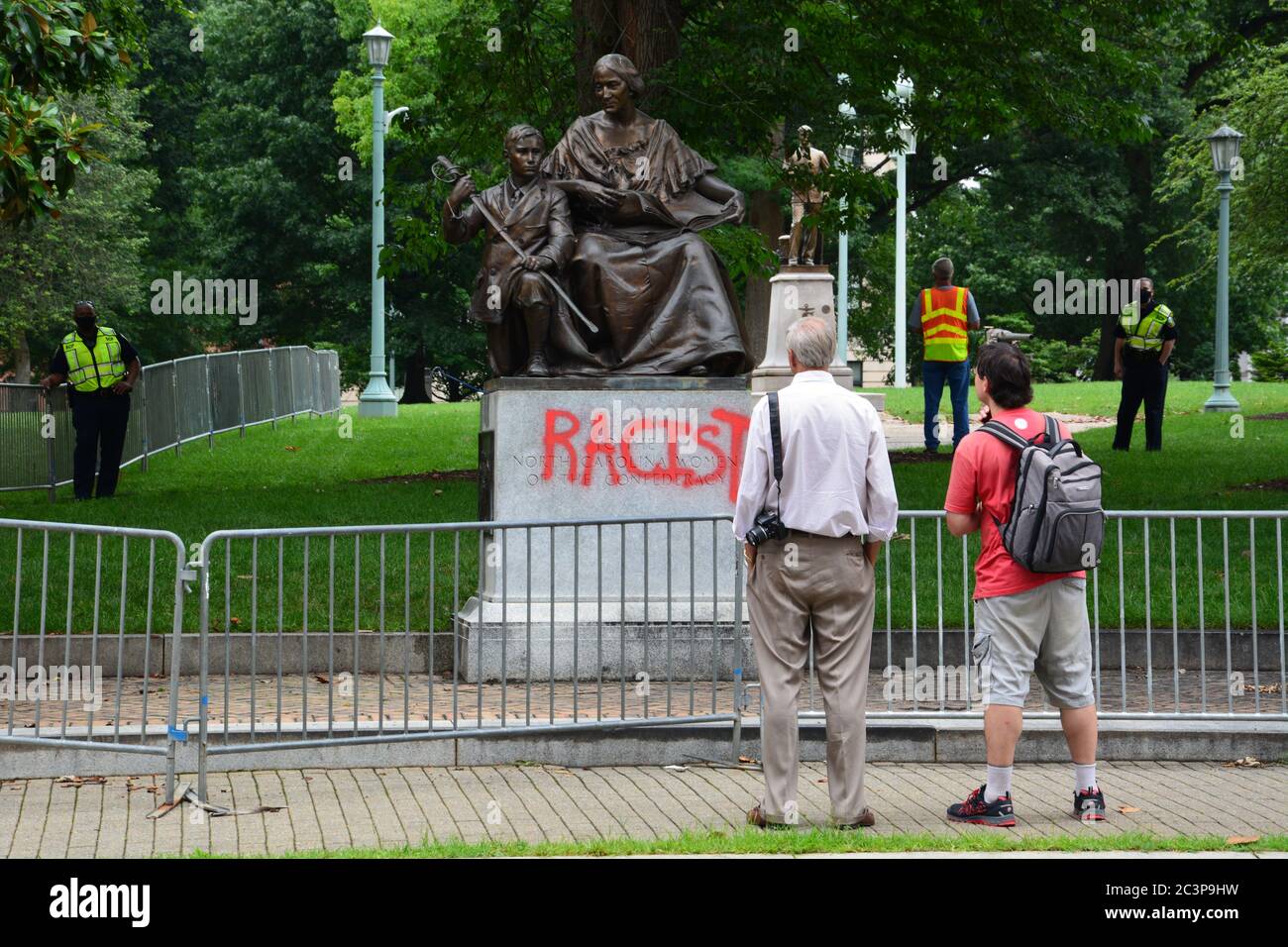 Raleigh, NC, Stati Uniti, 20 giugno 2020 - la gente si riunisce di fronte alla statua defaced che onora le donne della Confederazione mentre la parola si diffonde che sta venendo tolto. La decisione è giunta la mattina dopo che i dimostranti Juneteicenteschi, scatenati dall'uccisione della polizia di George Floyd, riescono a tirare due figure fuori della vicina colonna del Memoriale Confederato alta 70 piedi. La mattina del 20 il governatore del NC ordinò che fosse rimosso dai terreni del vecchio palazzo del Campidoglio e altri due monumenti confederati. Foto Stock