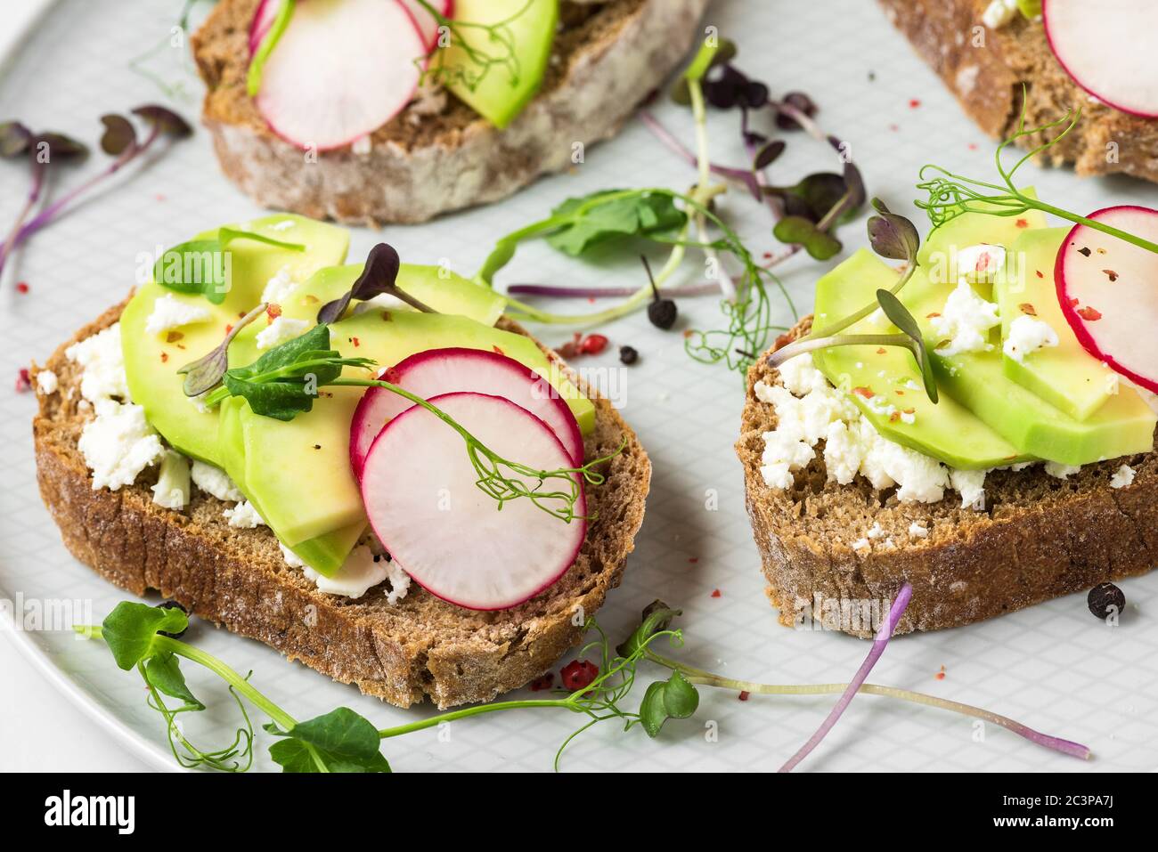 Salumi di avocado di primavera con ravanelli, formaggio di cottage, germogli di piselli e pepe per una sana colazione. Primo piano Foto Stock