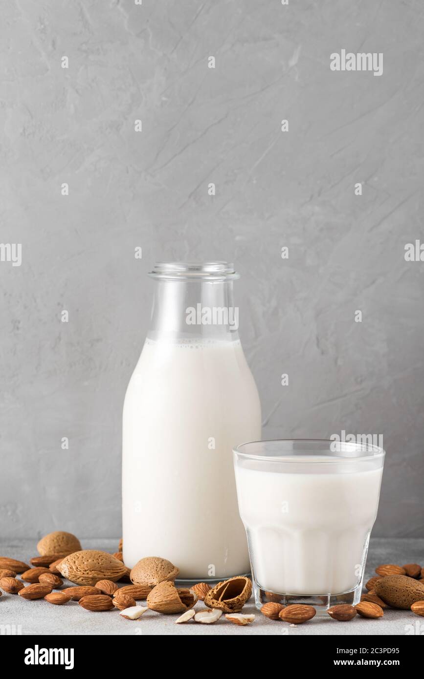 Latte di mandorle in bottiglia con bicchiere e mandorle su fondo di cemento. Latte vegetale privo di latte vegano. Orientamento verticale. Primo piano Foto Stock