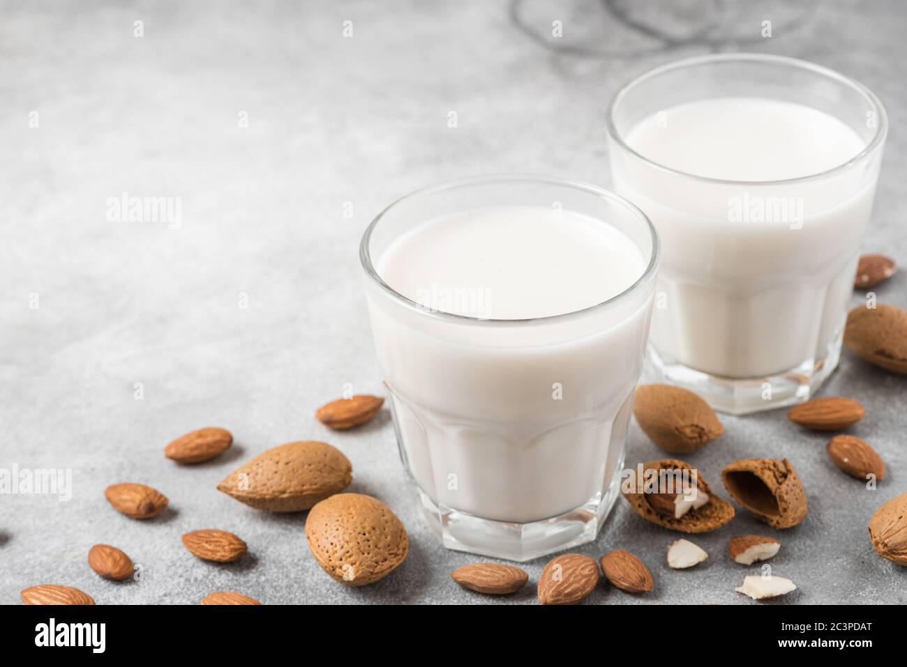 Latte vegano di mandorle a base vegetale in bicchieri con noci su fondo di cemento. Latte senza latte. Primo piano Foto Stock