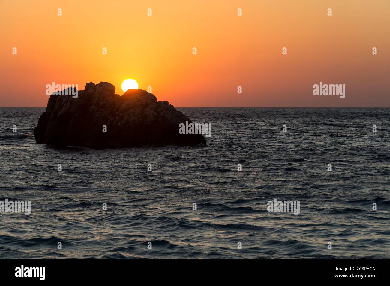 Tramonto mozzafiato sul mare ondulato con una roccia davanti, bagliore rosso nel cielo. Immagine orizzontale. Foto Stock