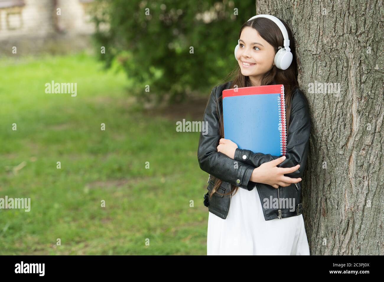 Lezioni di ascolto. Happy ragazza pratica di ascoltare le abilità all'aperto. I bambini piccoli si divertano ad ascoltare la musica. Ascolto corso. Apprendimento a distanza. Studio e formazione. Vita moderna. Scuola di lingua. Foto Stock