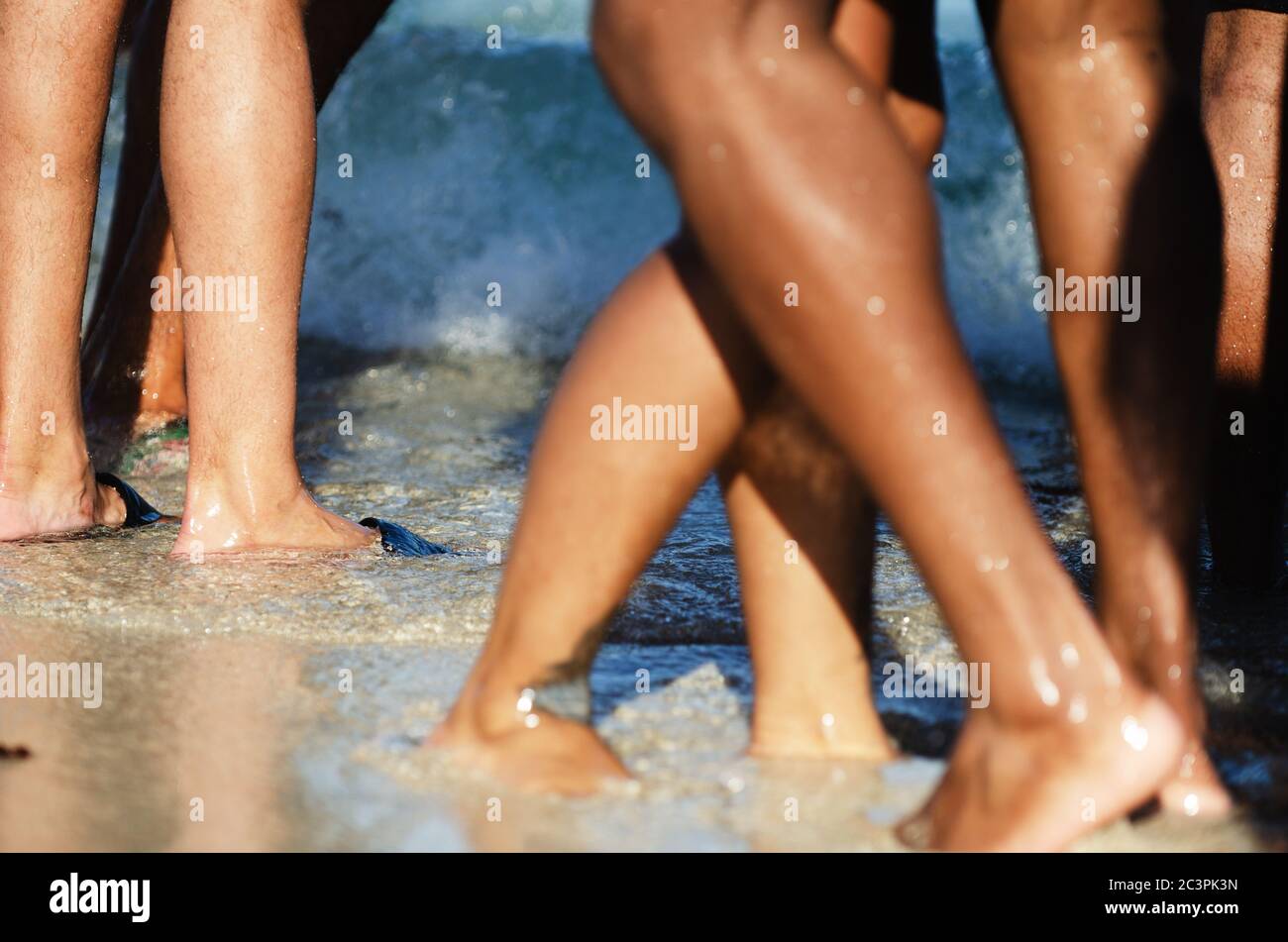 Primo piano delle gambe di giovani irriconoscibili che si godono la spiaggia in luce del sole dorata Foto Stock
