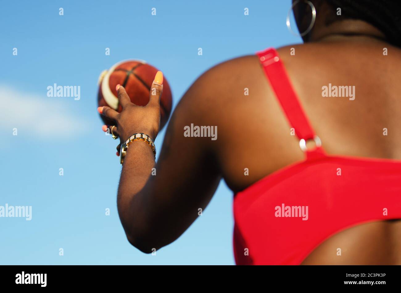 Donna afroamericana irriconoscibile che cattura un calcio sulla spiaggia contro il cielo azzurro soleggiato Foto Stock