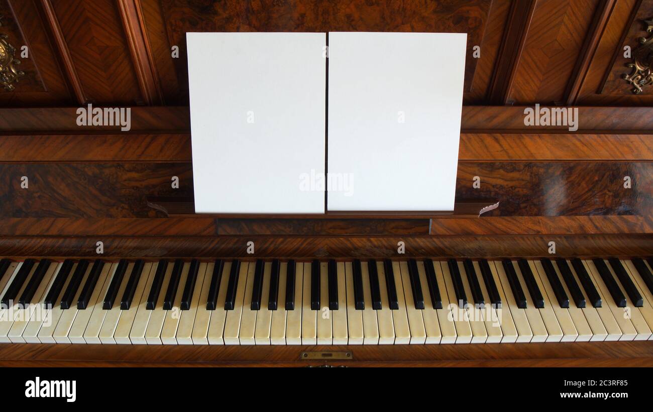 Vista frontale di un antico pianoforte in legno con la tastiera aperta e due fogli di carta bianca su supporto per note musicali Foto Stock