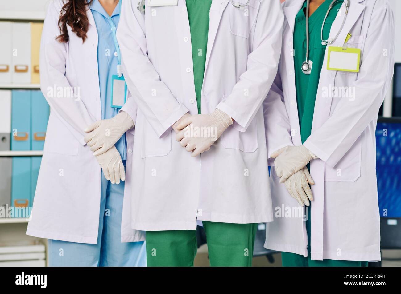 Immagine tagliata di medici in camici bianchi e guanti di gomma in piedi nella sala dell'ospedale Foto Stock