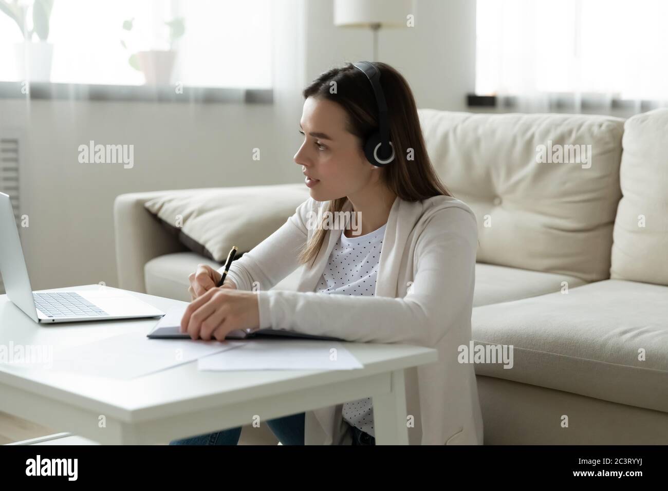 Donna concentrata in cuffie guardare webinar su notebook scrivere note Foto Stock