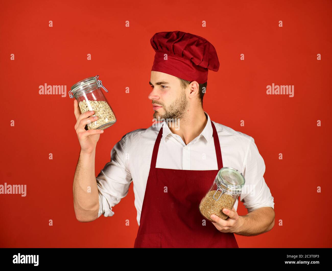 Chef con viso curioso tiene vasi con porridge su sfondo rosso. L