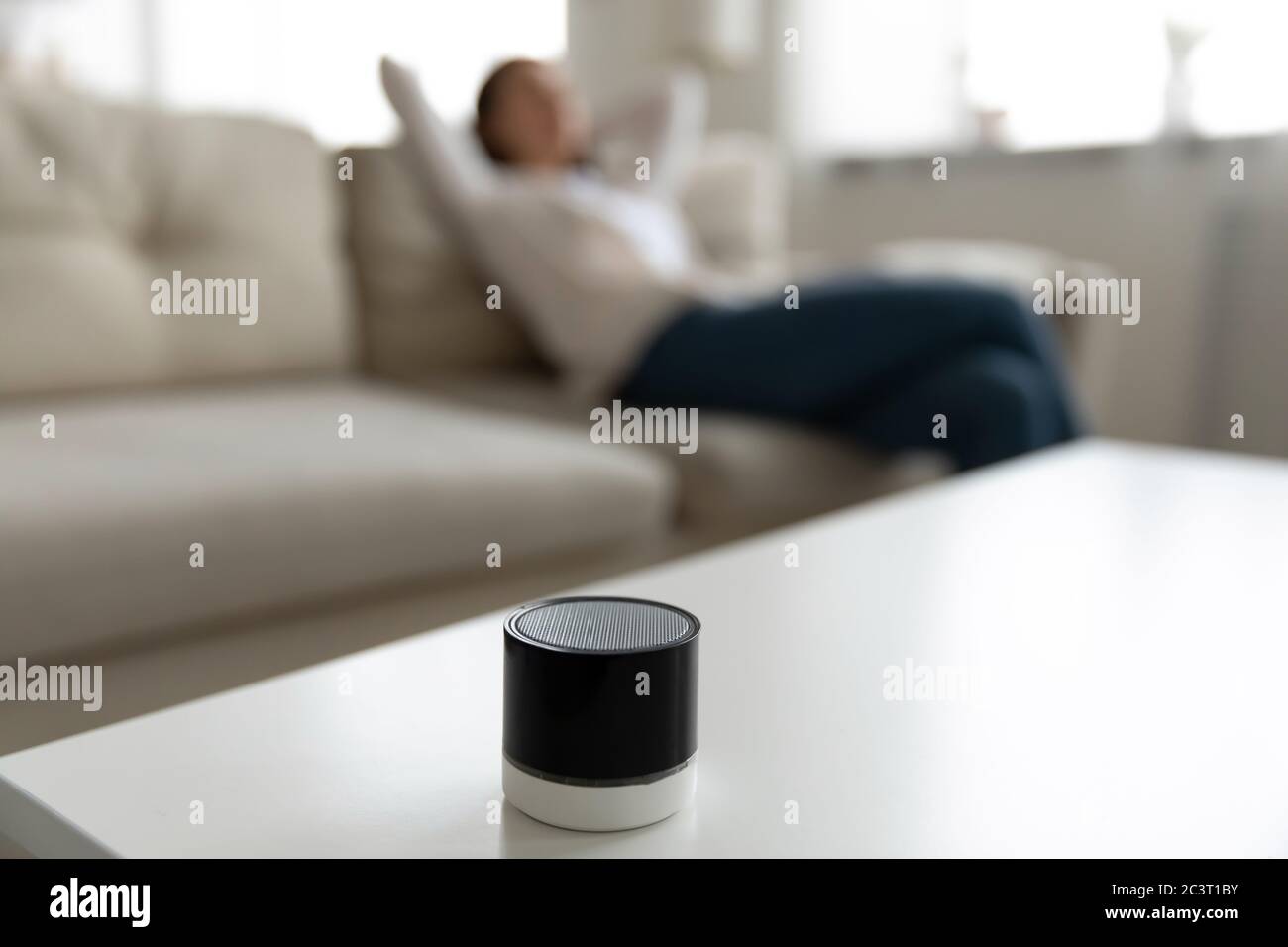 Donna che ascolta musica utilizzando un mini altoparlante portatile situato sul tavolo Foto Stock