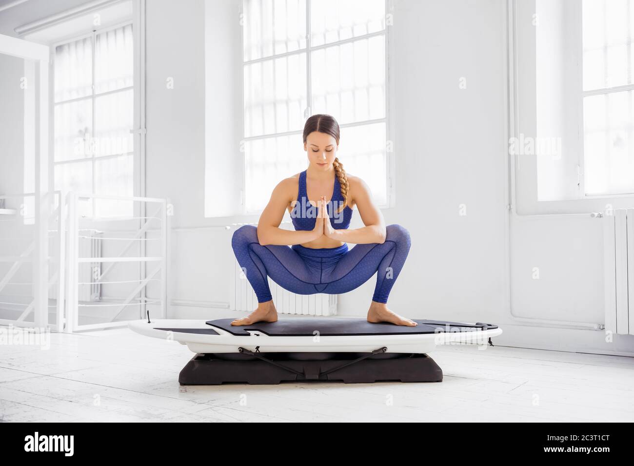Donna che fa un surf yoga ghirland posa su una tavola in una vista frontale in una palestra chiave in un concetto di salute e fitness Foto Stock