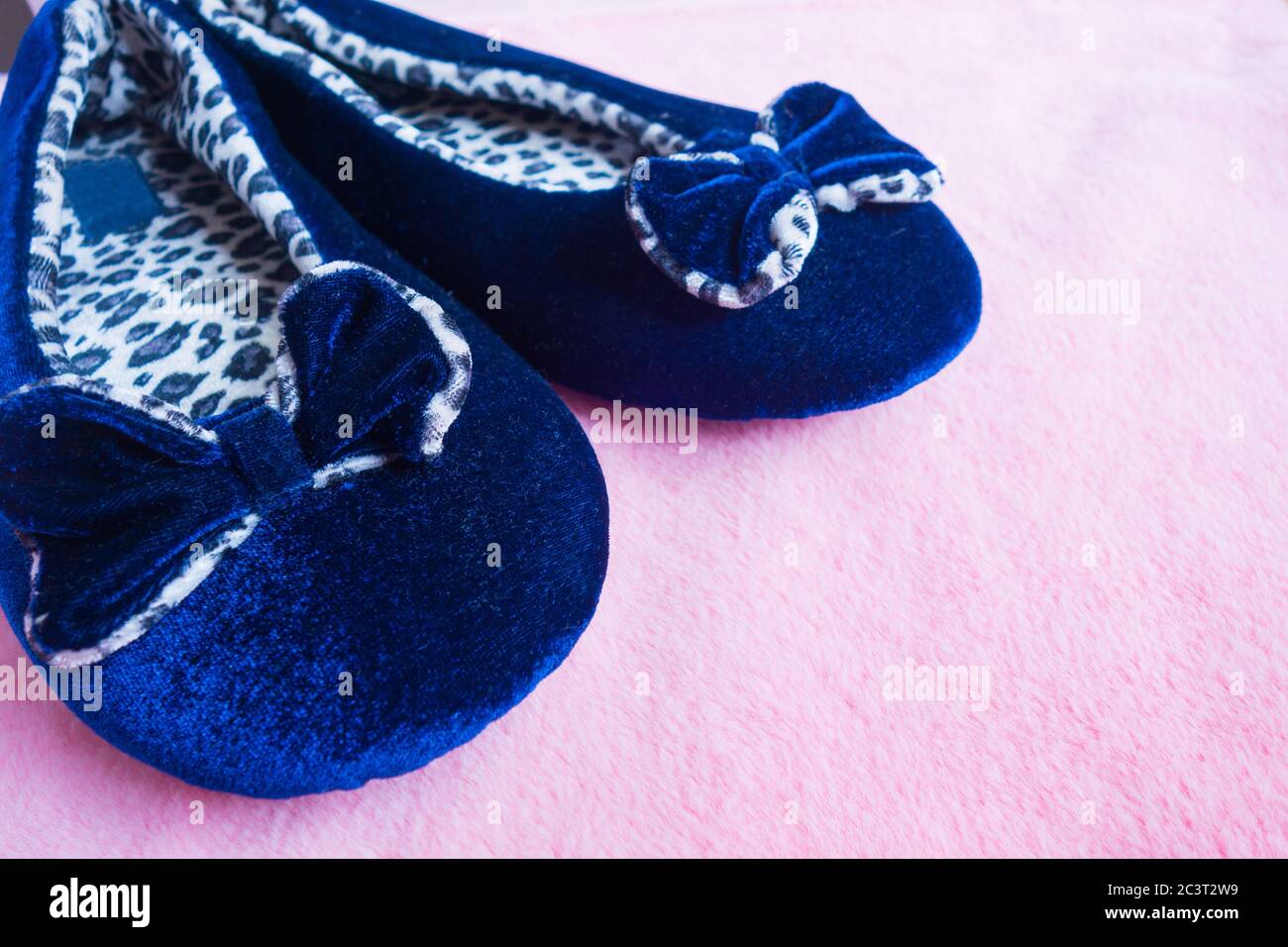 Pantofole color leopardo blu con prua su un soffice tappeto rosa. Abbigliamento domestico per donna o bambini. Il concetto di calore e comfort domestici. Messa a fuoco selettiva Foto Stock