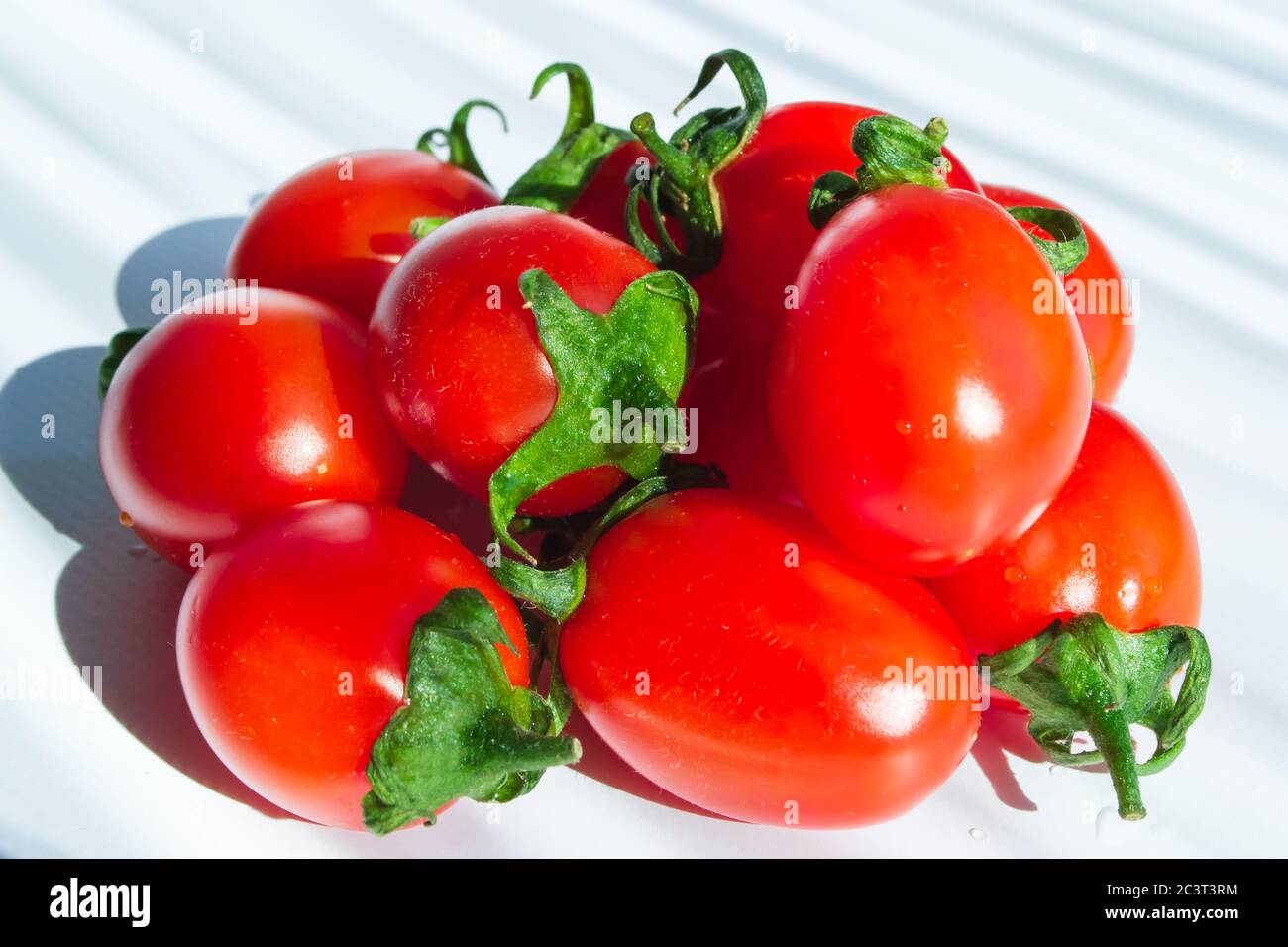 Pomodori ciliegini freschi con gambo verde su sfondo chiaro. Primo piano. Messa a fuoco selettiva Foto Stock