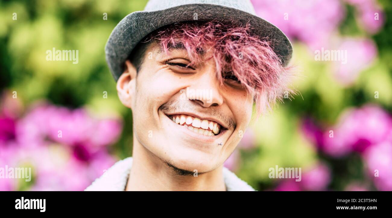 Felice allegro bel ritratto trendy alternativo giovane uomo adolescente sorridente su macchina fotografica con sfondo colorato parco di fiori - diversità e giovane Foto Stock