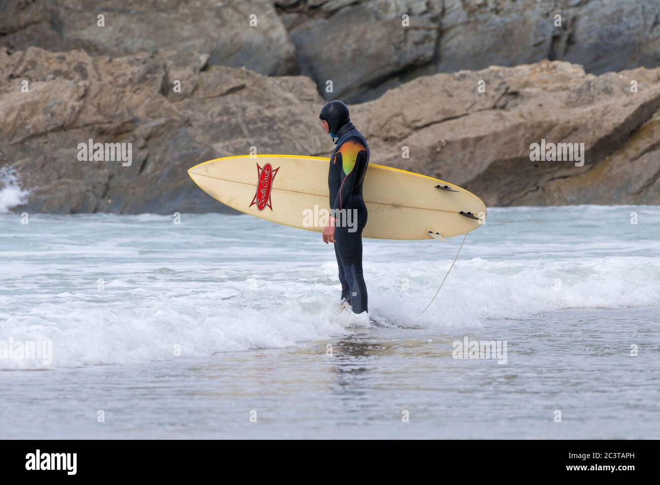 Un surfista si trova in piedi tenendo la sua tavola da surf e perso nel pensiero su Fistral Beach a Newquay in Cornovaglia. Foto Stock