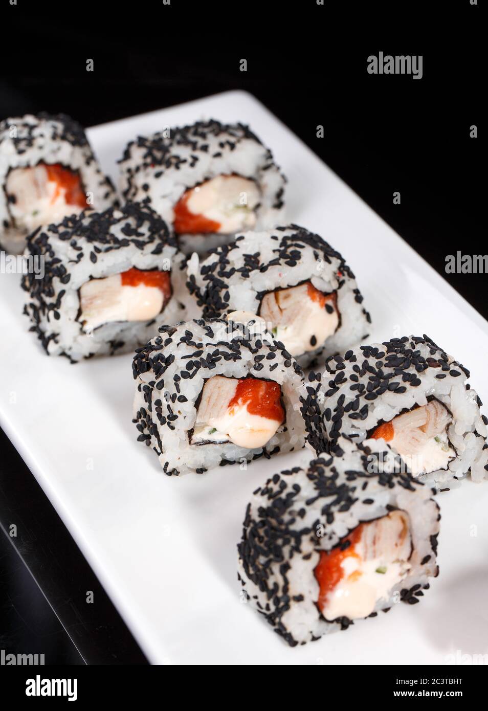 Rotolo di sushi uramaki con salmone, anguille affumicate, cetriolo, formaggio cremoso e semi di sesamo su un piatto bianco. Foto Stock