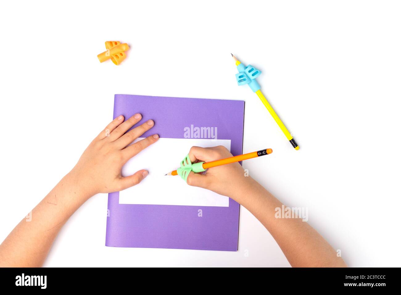 portamatite da training ergonomico, scrittura a mano con preschooler, bambini che imparano a tenere una matita, esercizi con le dita, ritorno a scuola, le mani dei bambini firmano un notebook Foto Stock