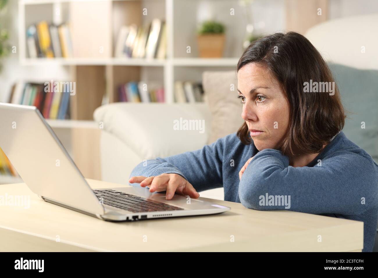 Donna adulta seria che controlla i contenuti online sul computer portatile seduto sul pavimento nel salotto di casa Foto Stock